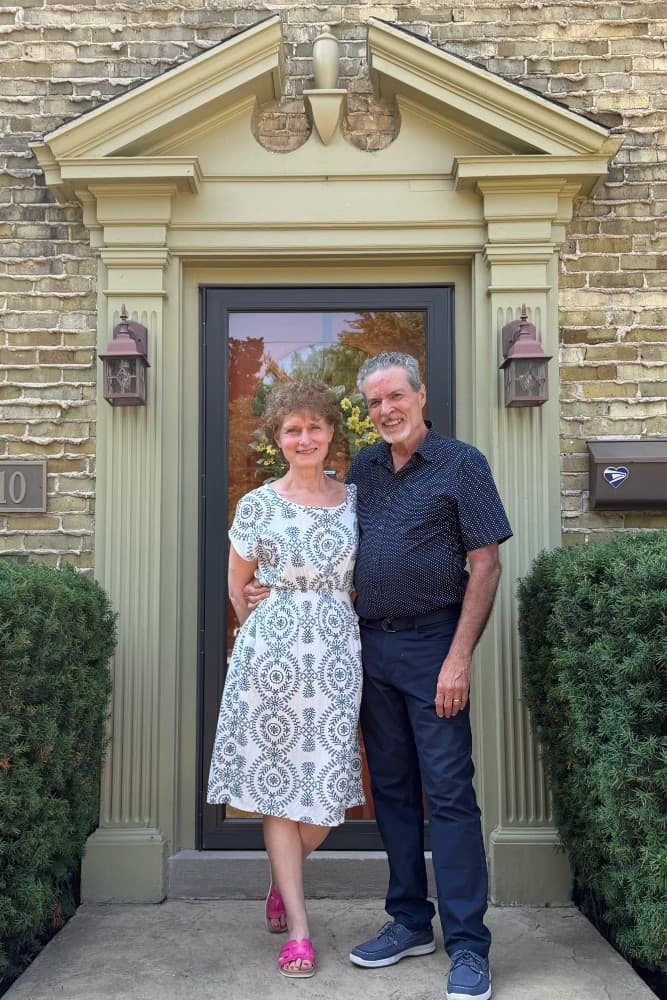 A couple stands together in front of a stylish home entrance, smiling warmly.