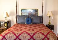 A neatly made four-poster bed with a patterned quilt, decorative pillows, and bedside lamps.