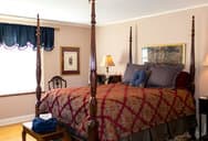A cozy bedroom featuring a four-poster bed, cream walls, and soft lighting.
