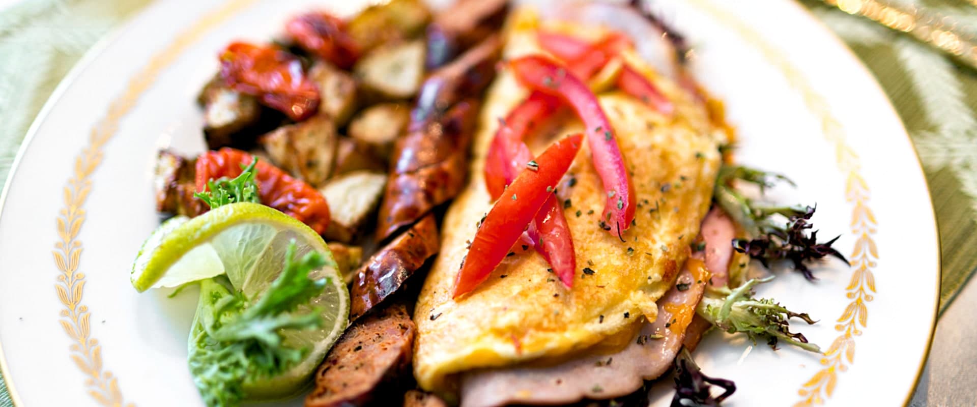 A plate of food featuring an omelet topped with red peppers, accompanied by roasted potatoes and greens.