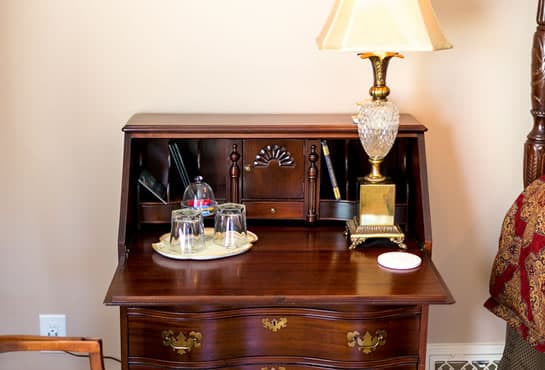 A wooden desk with a lamp, decorative item, and two glasses on a tray.