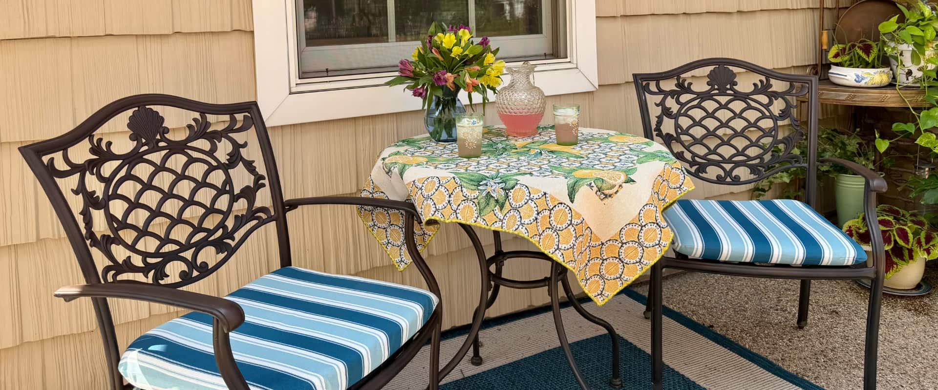 A cozy outdoor seating area with two patterned chairs and a small table adorned with a colorful tablecloth and floral arrangement.