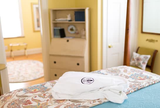 A neatly folded white robe sits atop a colorful quilt in a bright, cozy room with yellow walls and wooden furniture.