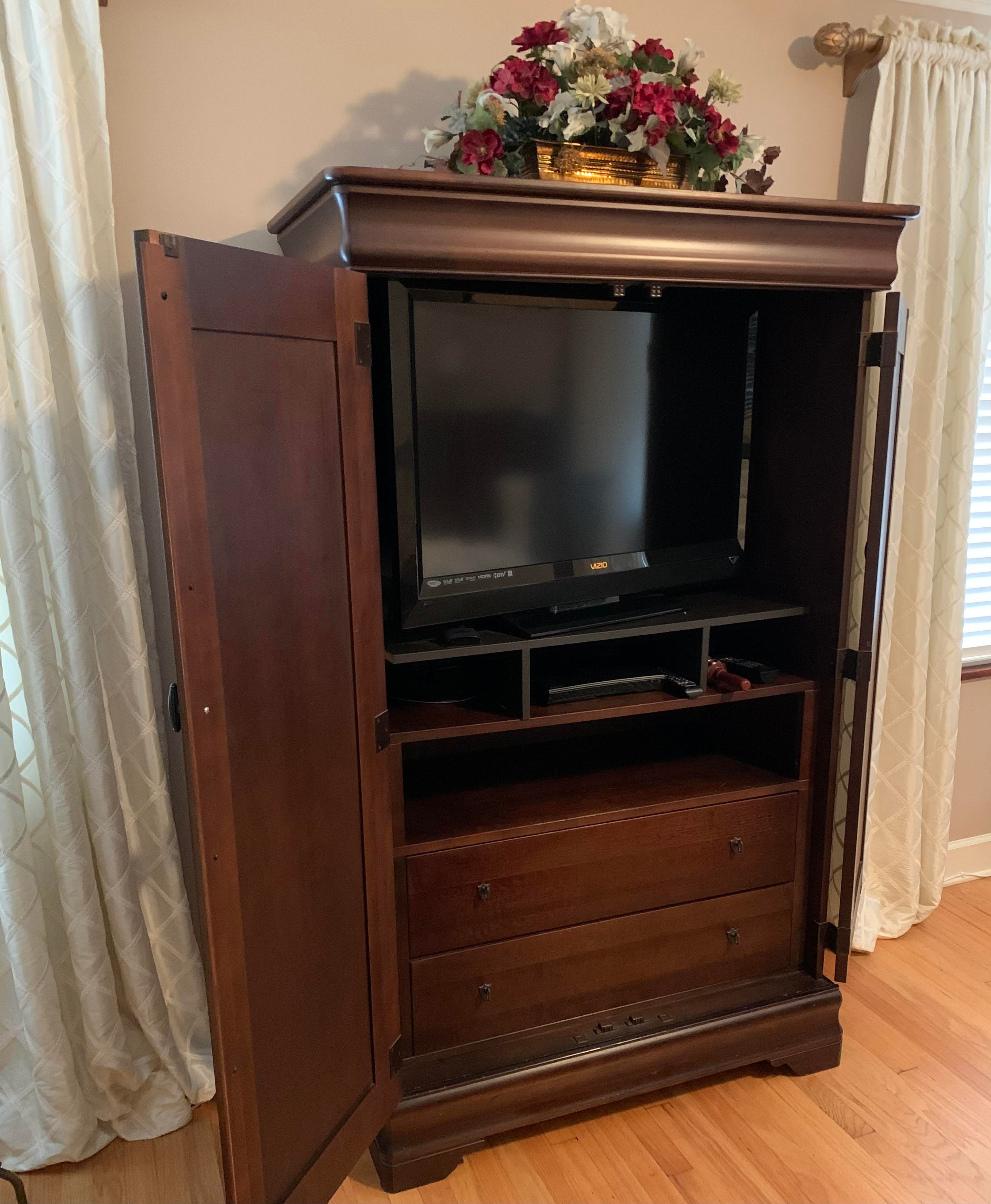 A wooden television armoire with a TV and two drawers, decorated with flowers on top.