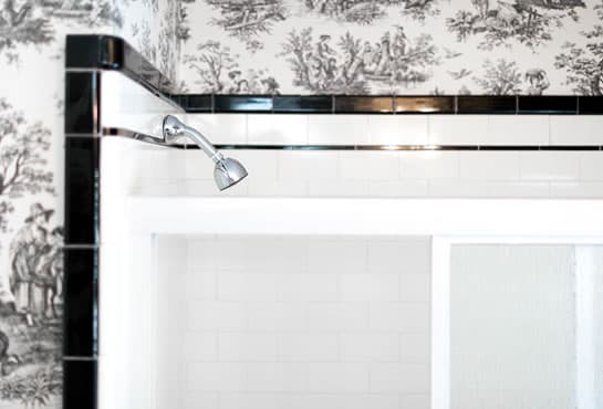 A chrome showerhead mounted above a white shower enclosure with a patterned wallpaper background.