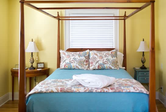 A cozy bedroom features a four-poster bed with colorful bedding and lamps on either side.